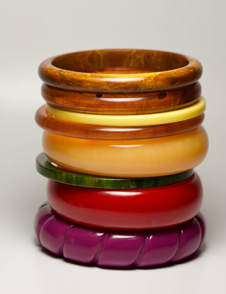 Close up view of vintage bakelite bangle bracelets in varying colors and widths on white background