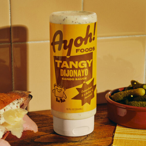 Ayoh! Foods squeeze bottles feature vibrant retro color palettes with playful hand-drawn mascot characters and vintage diner-inspired typography that channels classic American sandwich shop aesthetics. The design system celebrates nostalgic deli culture through bold graphic elements and whimsical illustrations, transforming premium condiments into approachable comfort food essentials. Design by Center.